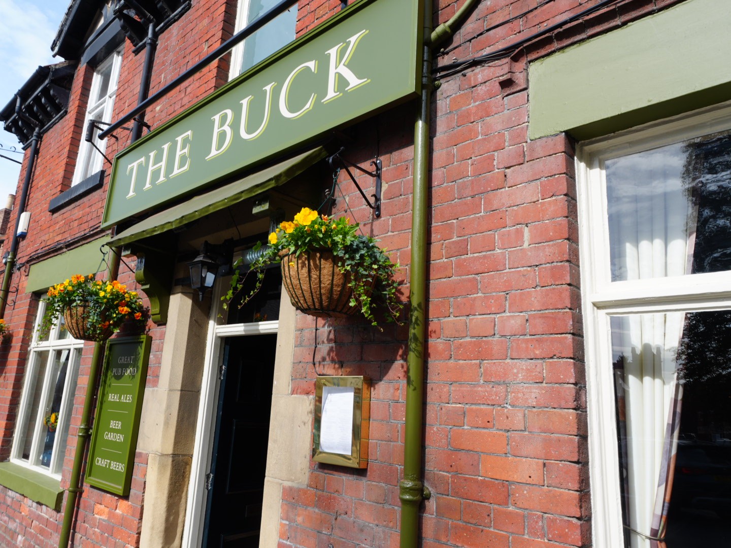 The green sign and hanging flower baskets above the entrance of The Buck Inn in Thornton-le-Dale