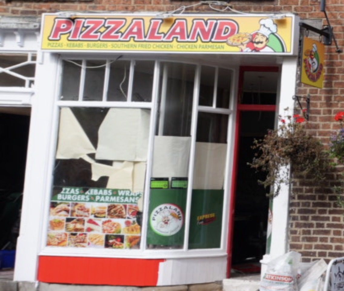 The Pizzaland shopfront on Pickering Road in Thornton-le-Dale, with a yellow fascia sign in red lettering showing a cartoon chef holding a pizza, and windows listing pizzas, kebabs, wraps, burgers and parmesans