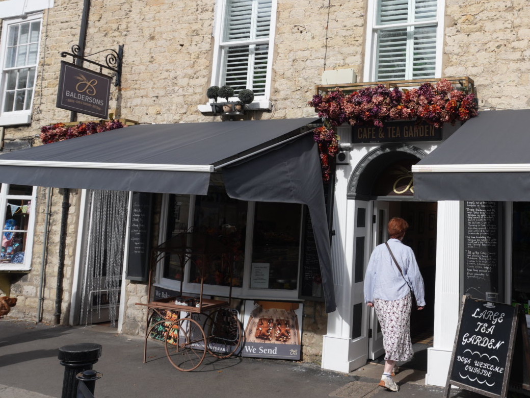 The Baldersons café frontage in Thornton-le-Dale, with a CAFÉ & TEA GARDEN sign above the arched doorway, grey awnings over the windows and a Large Tea Garden A-board outside
