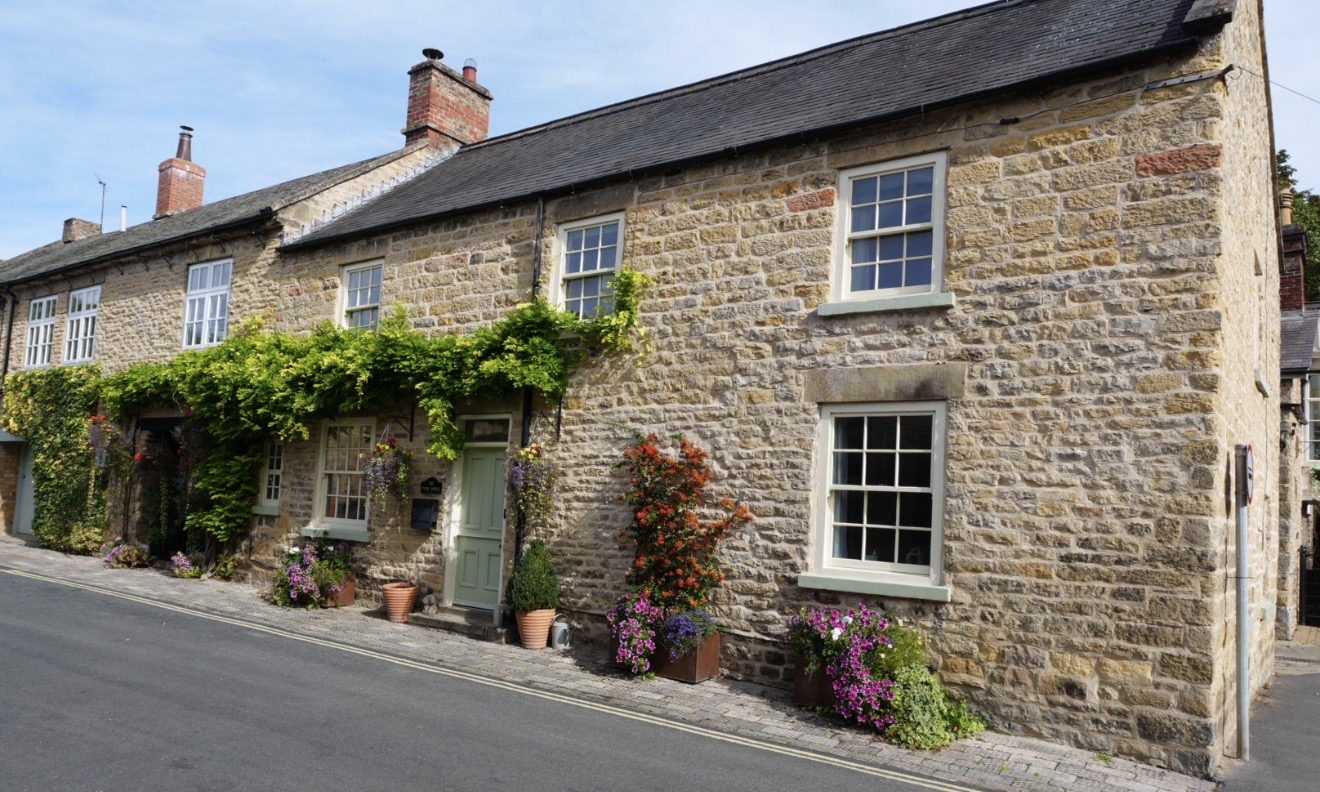 A row of stone cottages with wisteria over the doors and flower pots on the pavement