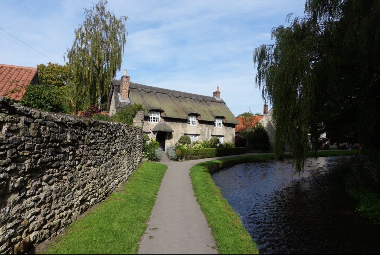 A path between a stone wall and Thornton Beck leading to the thatched Beck Isle Cottage