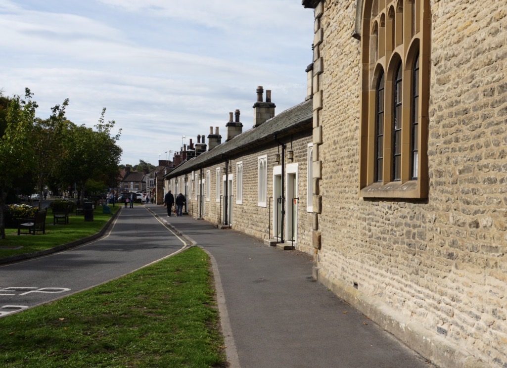 The long stone row of the almshouses beside the road, with the green on the left