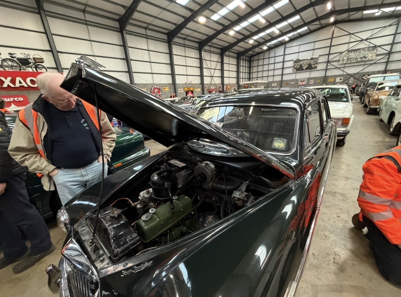 Dark green Jaguar with its bonnet raised and engine visible as visitors look around inside Mathewsons