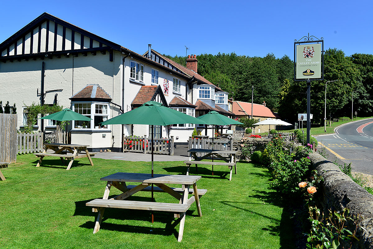 The hanging sign and front garden of the Cayley Arms at Allerston, with picnic tables and green umbrellas on the lawn