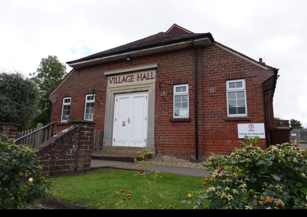 A red-brick building with a Village Hall sign above the door