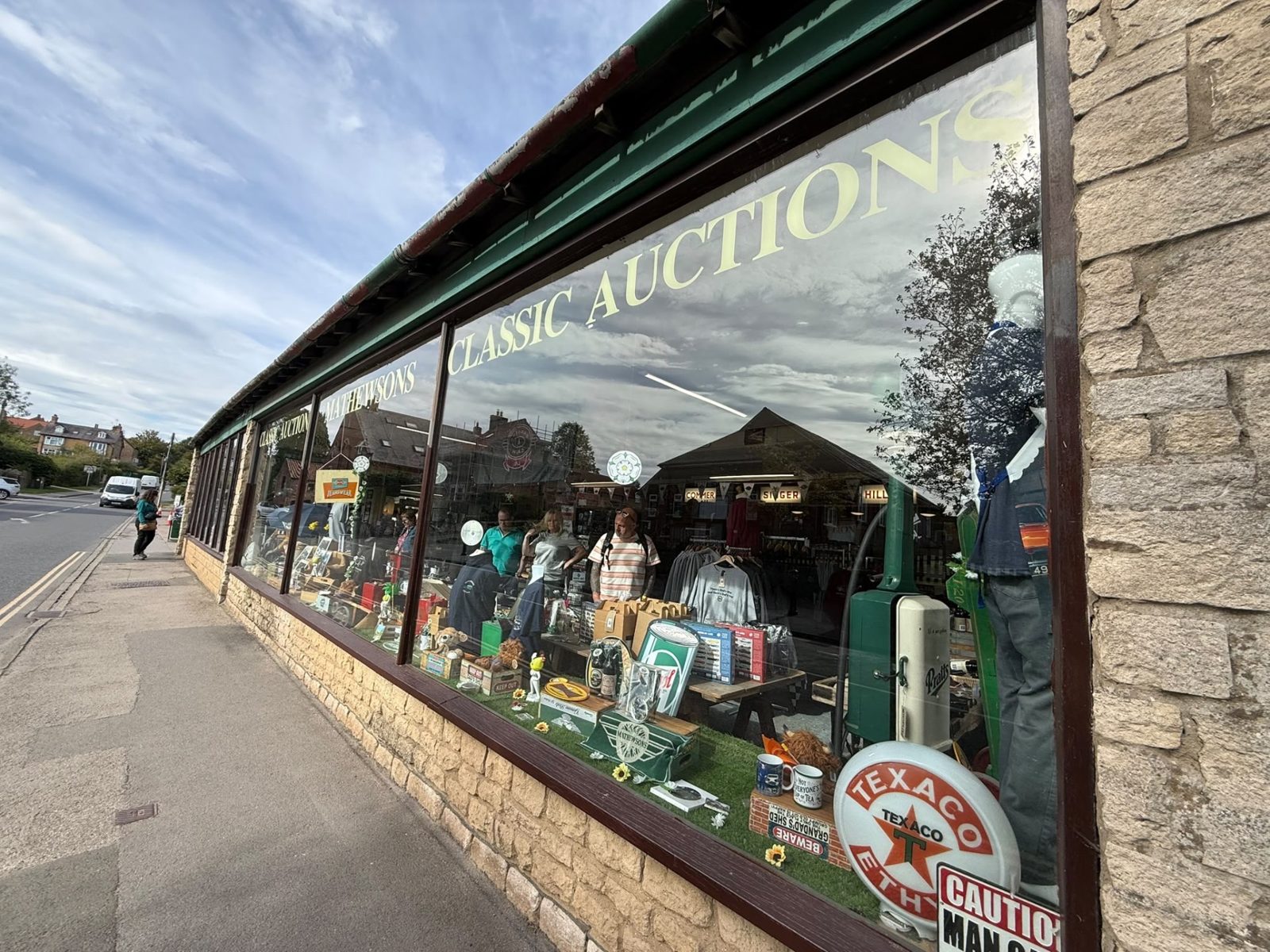 The long shop window along the Pickering Road pavement, lettered Classic Auctions, with a Texaco sign and mannequins in Mathewsons clothing behind the glass