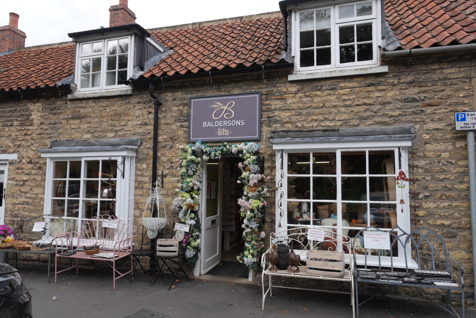 The Baldersons gift shop in Thornton-le-Dale, a stone shopfront with bay windows, a flower-garlanded door and metal garden furniture outside