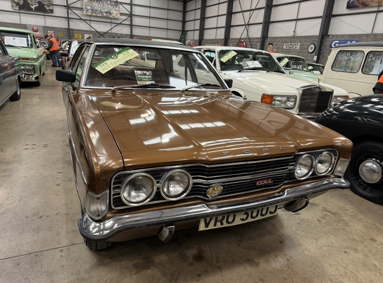 Front view of a bronze Ford with four round headlights among the cars inside Mathewsons