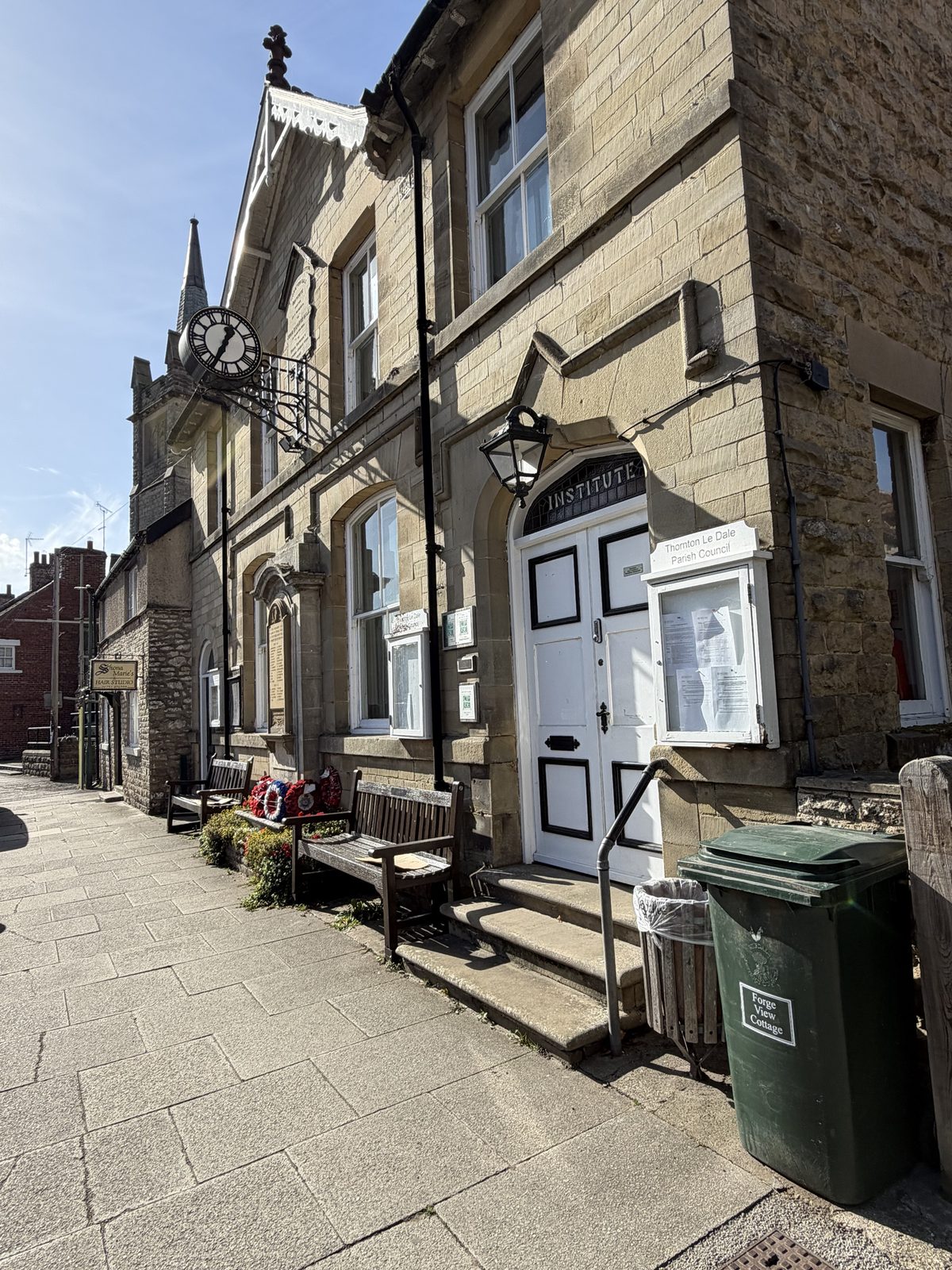 A stone building with a clock and noticeboards on a paved street