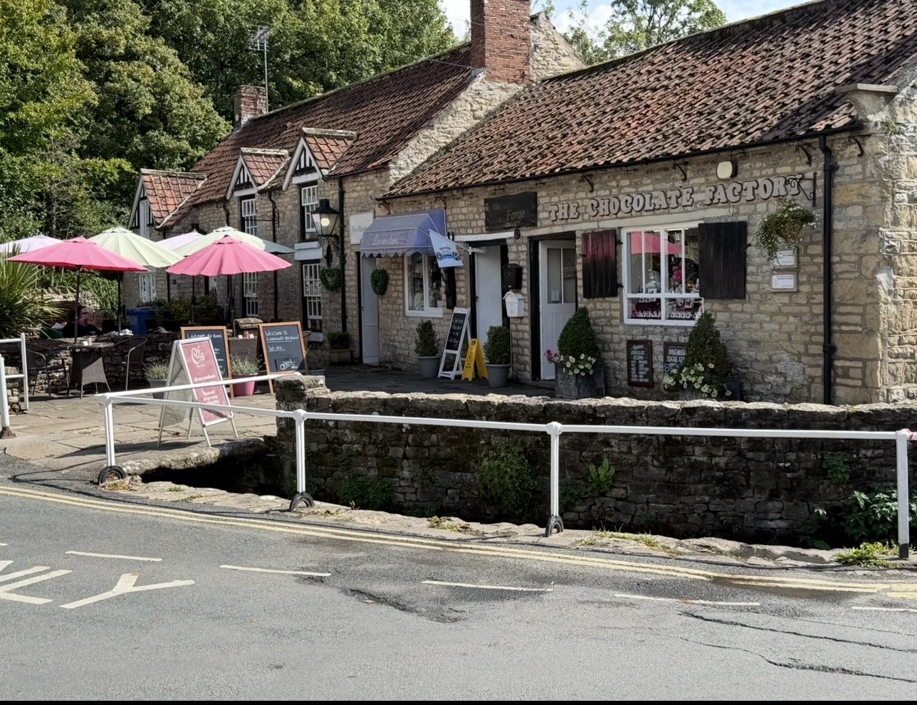 Stone cottages with parasols and a tea garden beside the road and the beck