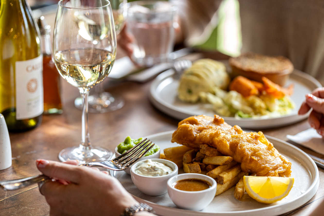 Beer-battered fish and chips with mushy peas, tartare sauce and a wedge of lemon, with a pie and a glass of white wine behind