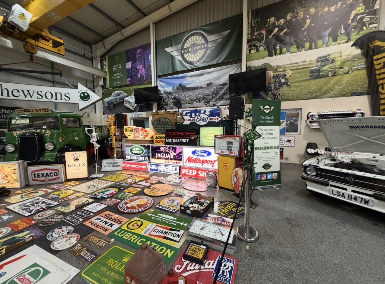 White Triumph Stag with its bonnet raised beside motoring signs, petrol pumps and memorabilia inside Mathewsons