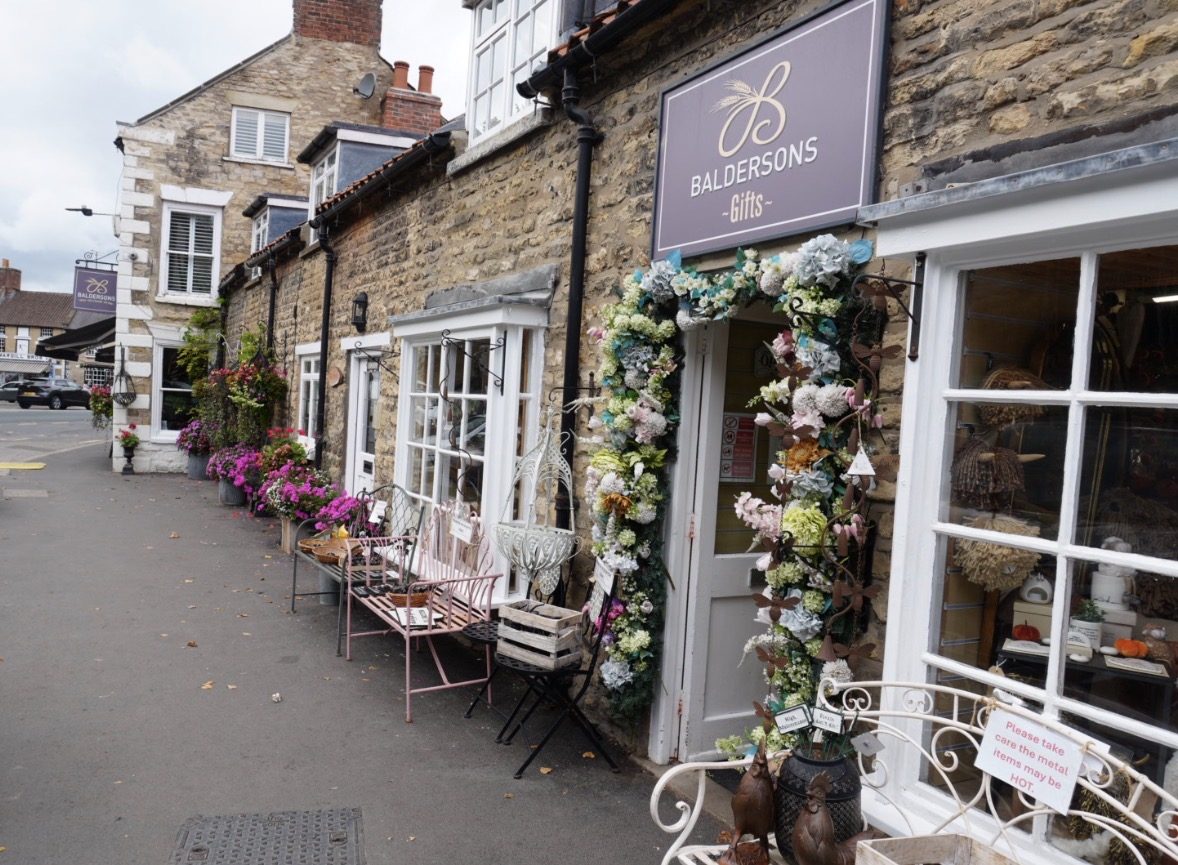 Baldersons Gifts with a flower arch around the door and benches outside, looking along the street