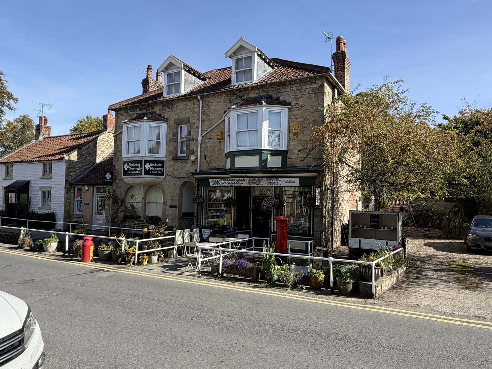 A stone building with Beckside Pharmacy and Moore's Delicatessen, and a red post box beside the railings