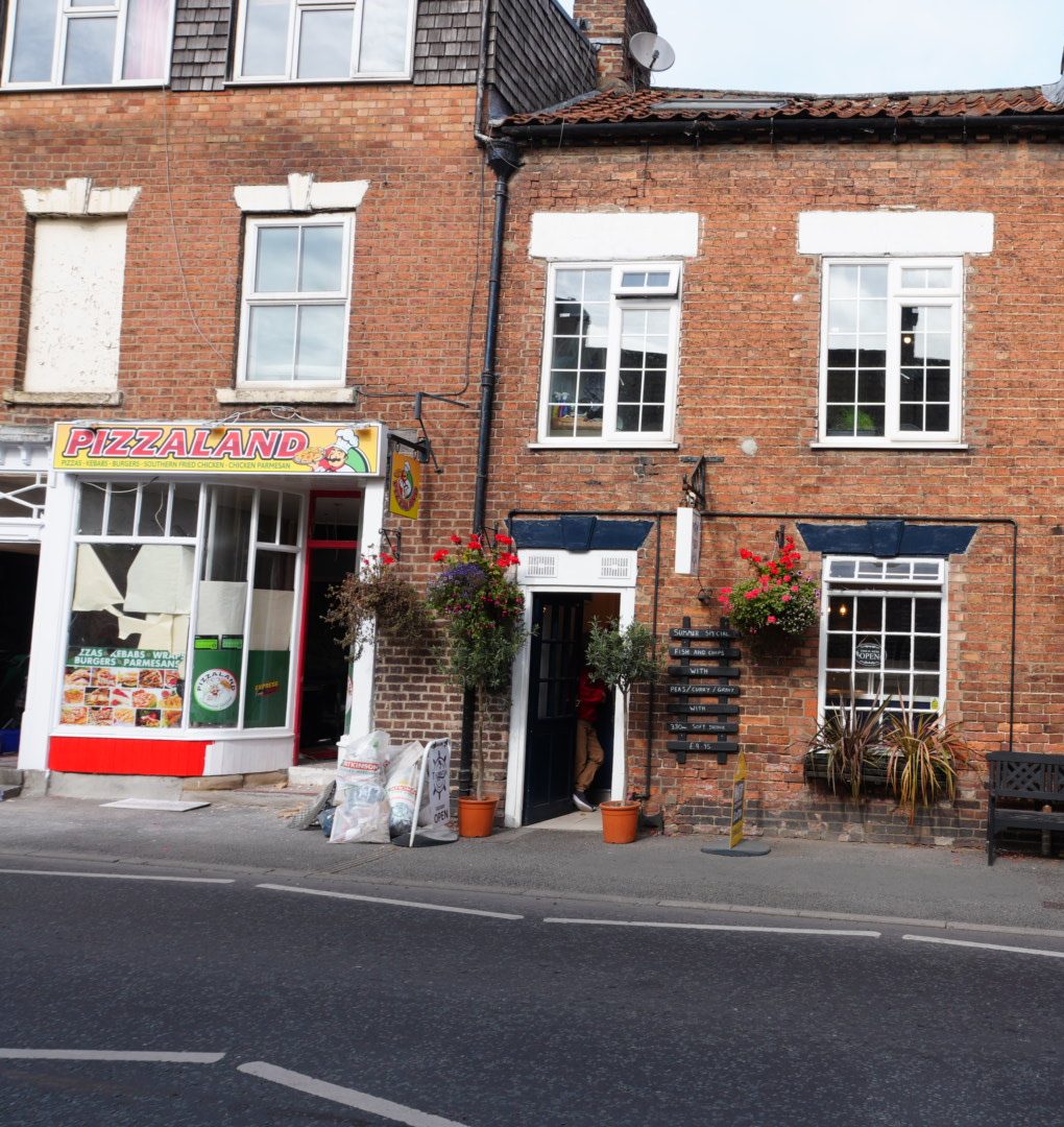 The Pizzaland shopfront and the chip shop next door, with hanging baskets