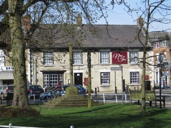 The New Inn behind the green and the medieval market cross in Thornton-le-Dale, a stone inn with a red sign