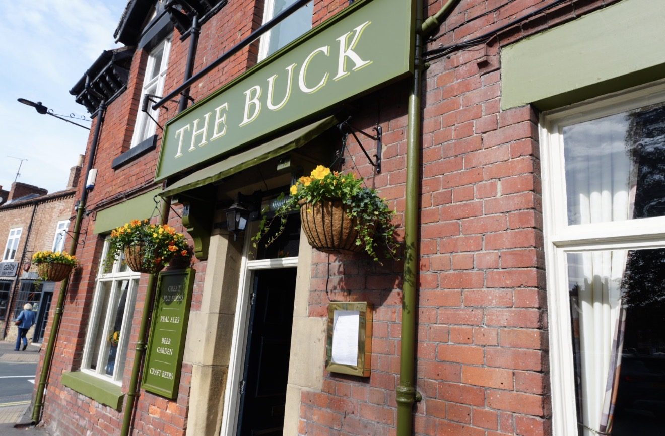 The sign and hanging baskets of The Buck pub