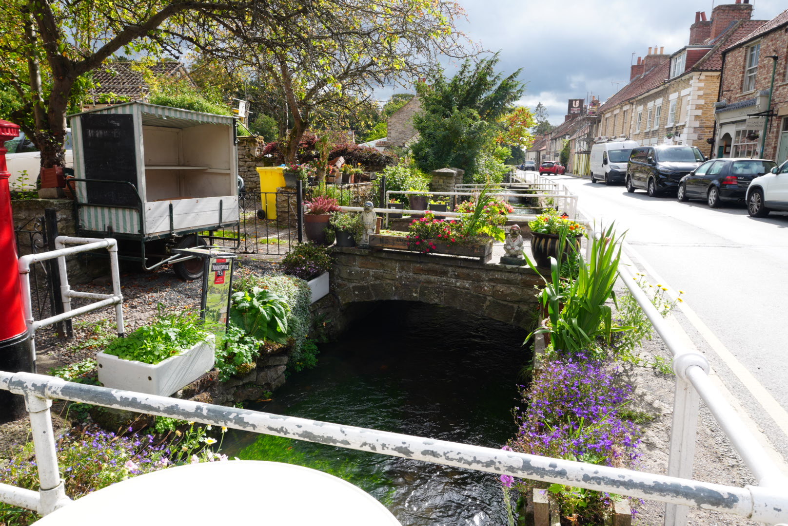 Flowers, planters and a striped tea cart beside Thornton Beck where it runs along Thornton-le-Dale's main street