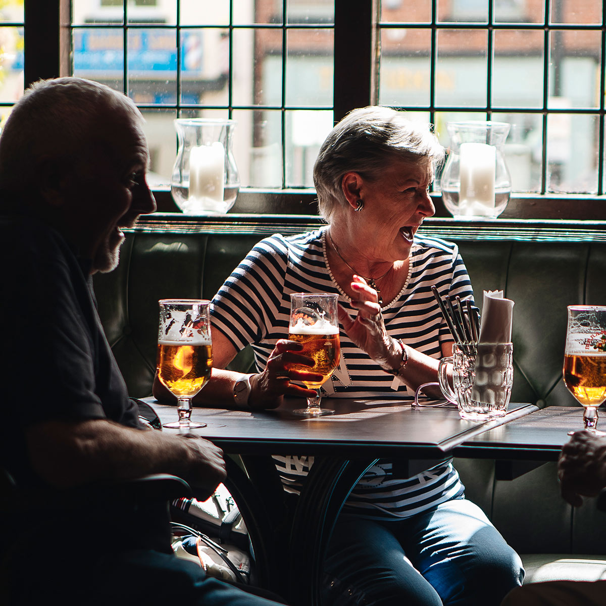 Two people talking over pints of beer at a window table inside The Buck